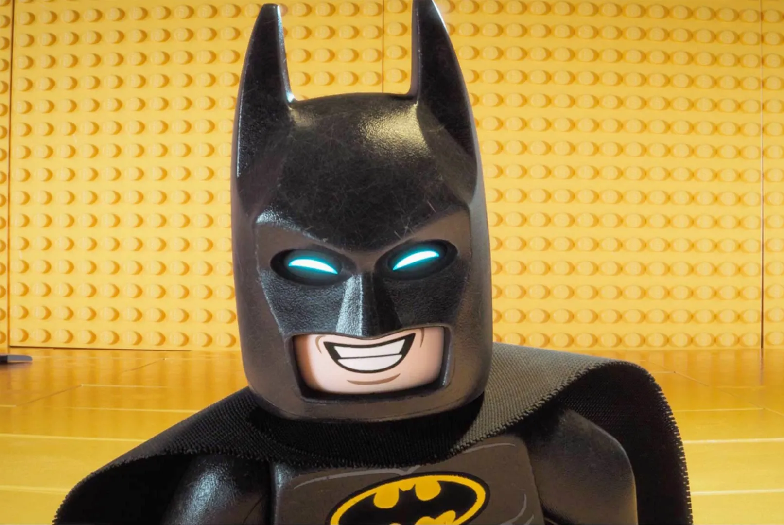 LEGO Batman grinning in front of a yellow LEGO wall